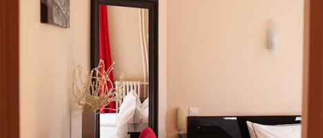 A hotel room with a bed, a desk, a chair, a mirror, and a vase with dried branches.