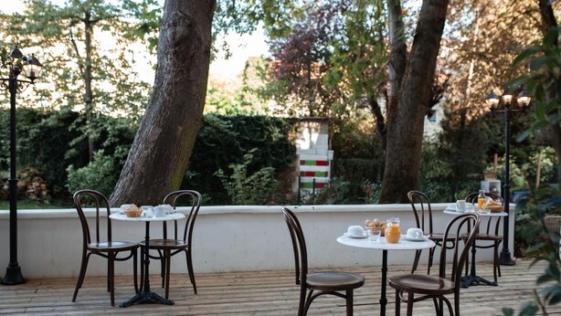 Un espace de restauration en plein air, avec des tables et des chaises en bois, entouré d’arbres et de verdure.