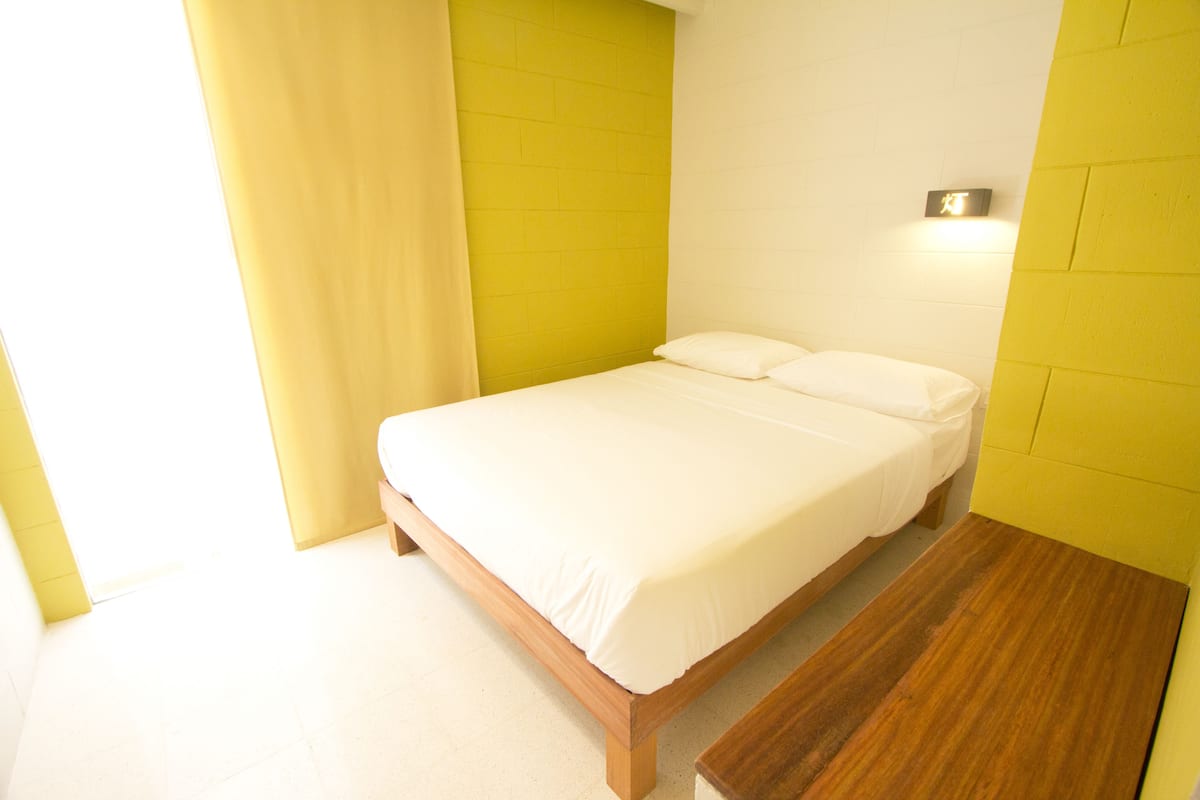 A single bed in a room with yellow walls and a wooden bench.