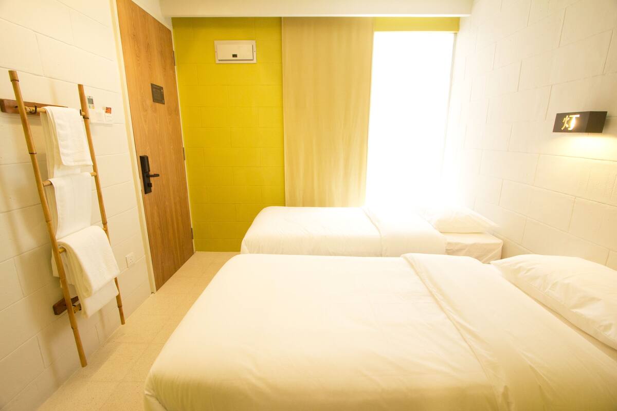 A hotel room with two beds, a wooden door, a yellow accent wall, and a window with a curtain.