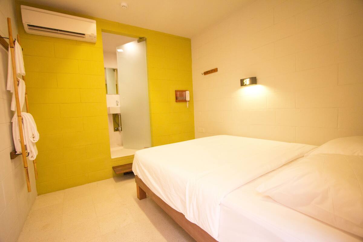 A hotel room with a bed, a bathroom, and a yellow wall.