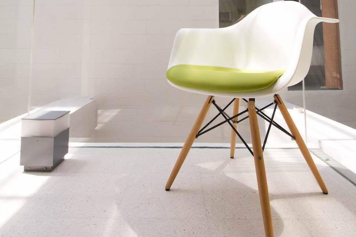 A modern interior with a white chair with green cushions, a glass wall, and a hanging flower arrangement.