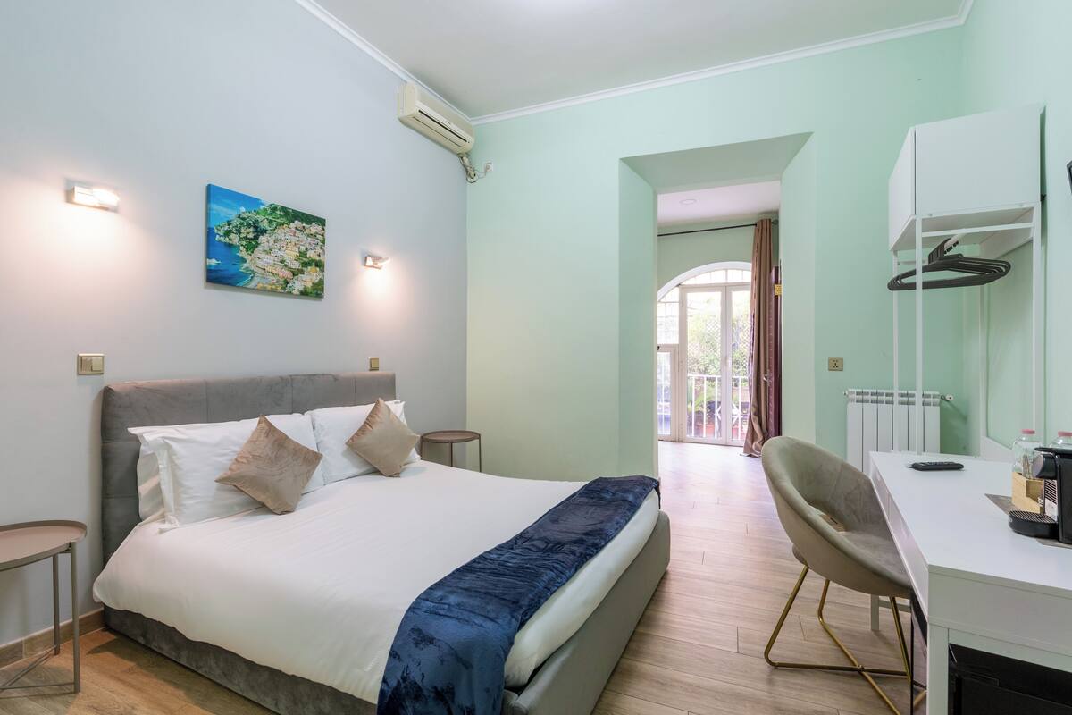 Une chambre d’hôtel moderne, équipée d’un lit, d’un bureau et d’une chaise. Un tableau orne le mur et un appareil de climatisation est installé au-dessus du lit.