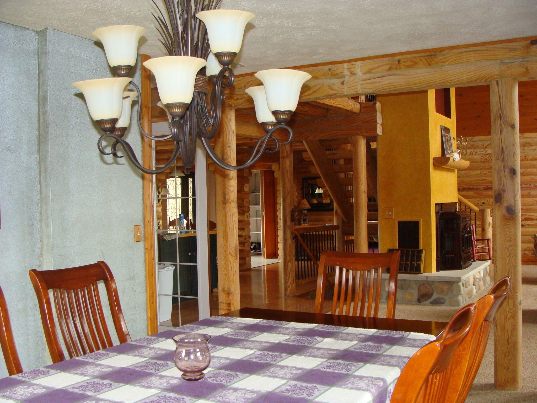 Uma sala de jantar com toalha xadrez, cadeiras de madeira e um candelabro.