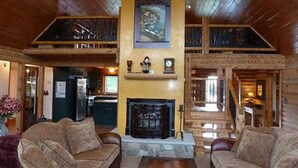 A log cabin interior with a fireplace, wooden ceiling, and a dining area visible in the background. - A Breath of Heaven B&B (Traverse City)