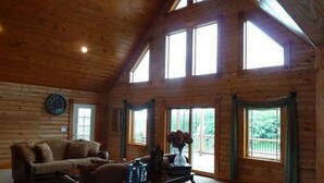 A log cabin interior with a high ceiling, large windows, a sofa, and a table with a vase. - A Breath of Heaven B&B (Traverse City)