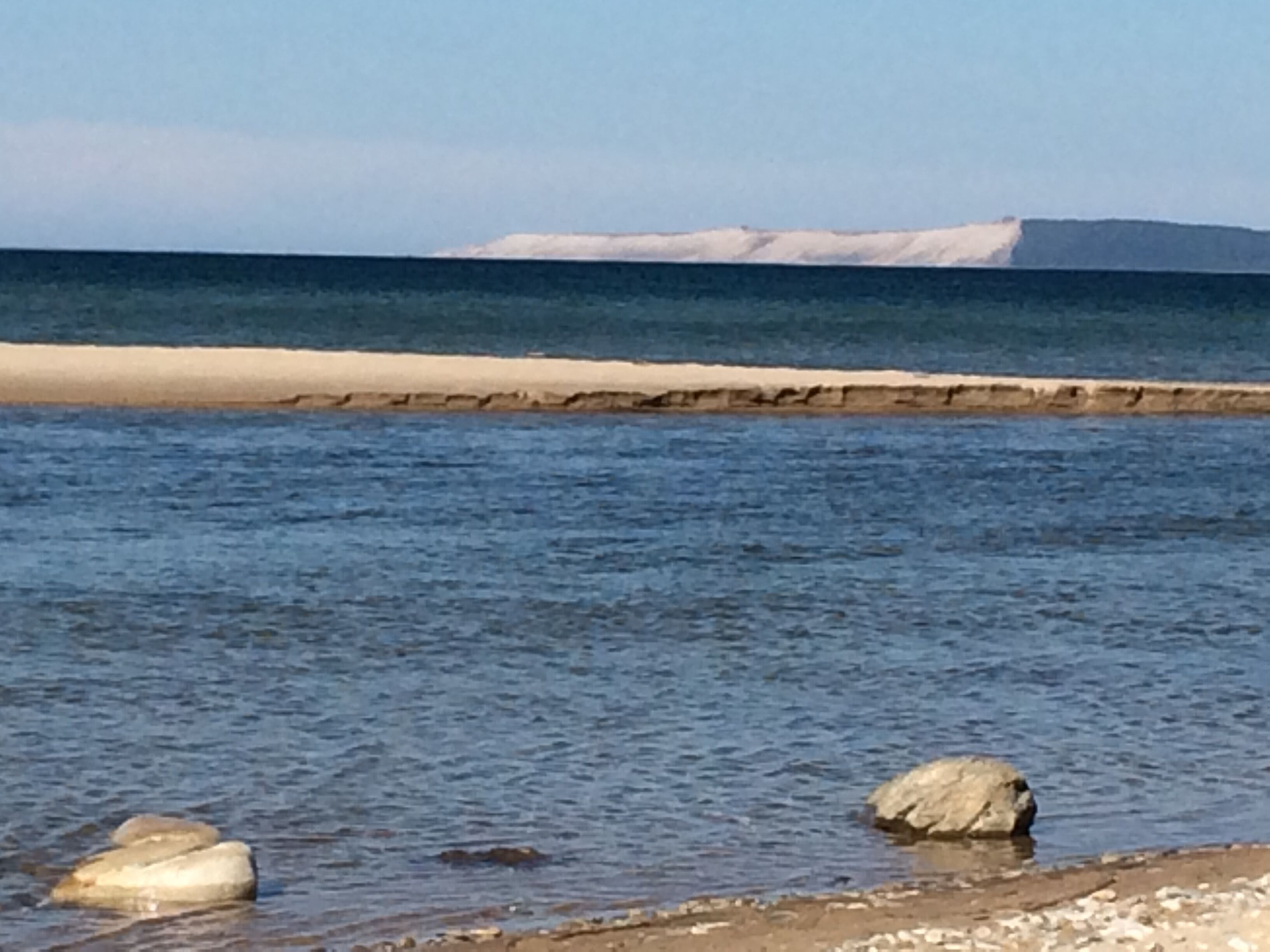 A coastal scene with calm water, rocks, and a distant shoreline.