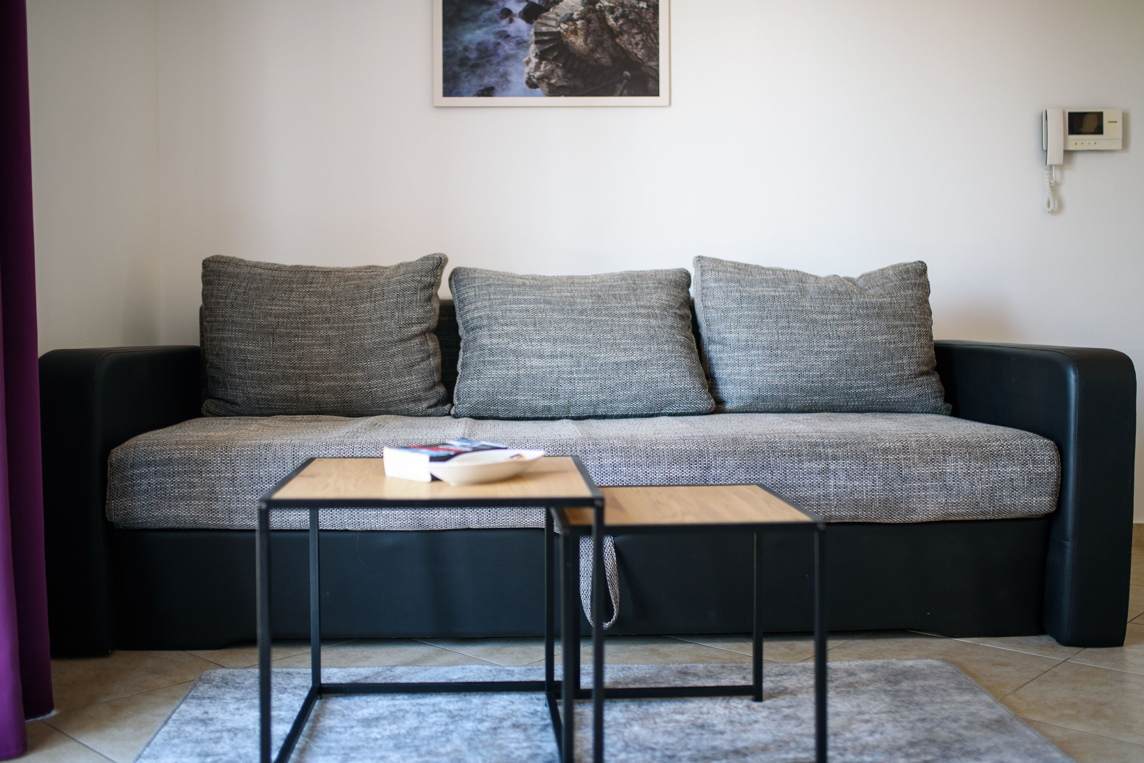 Un salon moderne avec un canapé gris, deux coussins gris, une petite table basse en bois et un tapis gris.