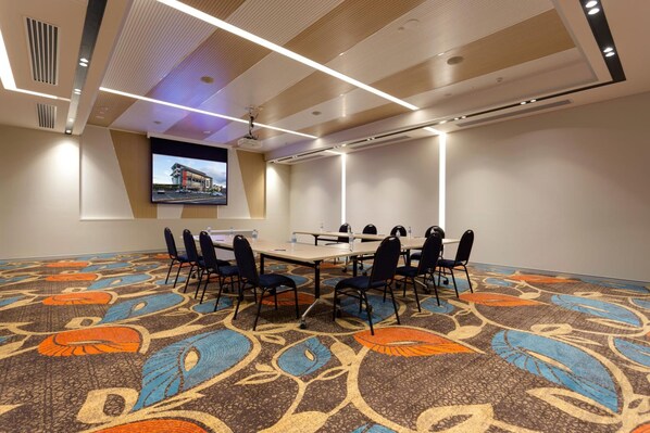 Una sala de conferencias con una mesa grande, sillas, una pantalla de proyector y una alfombra estampada.