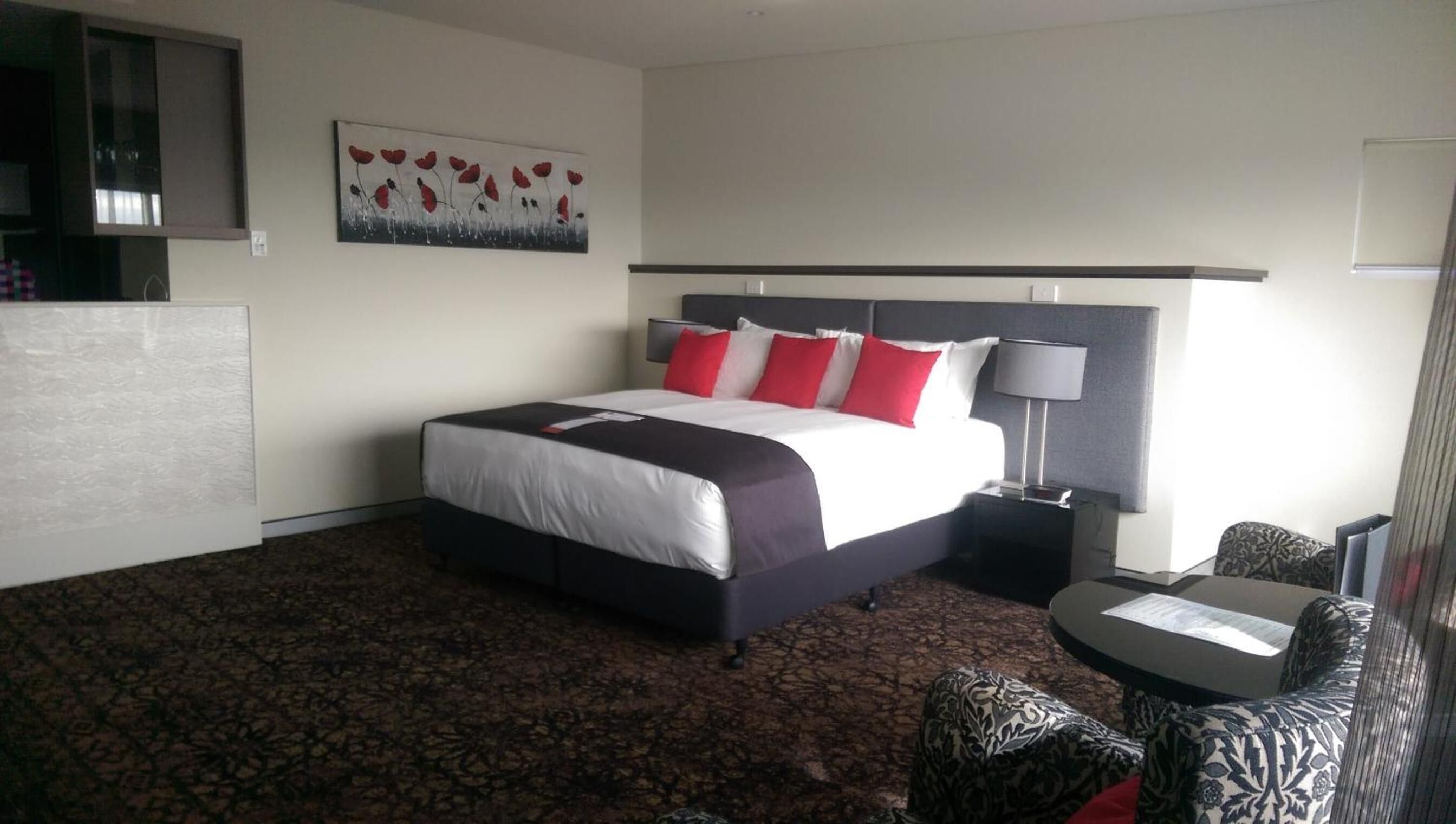 A hotel room with a bed, a nightstand, a chair, a desk, and a painting on the wall.