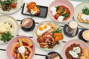 Verschiedene Frühstücksgerichte auf einem Tisch, darunter Eier, Speck, Würstchen und Pfannkuchen.