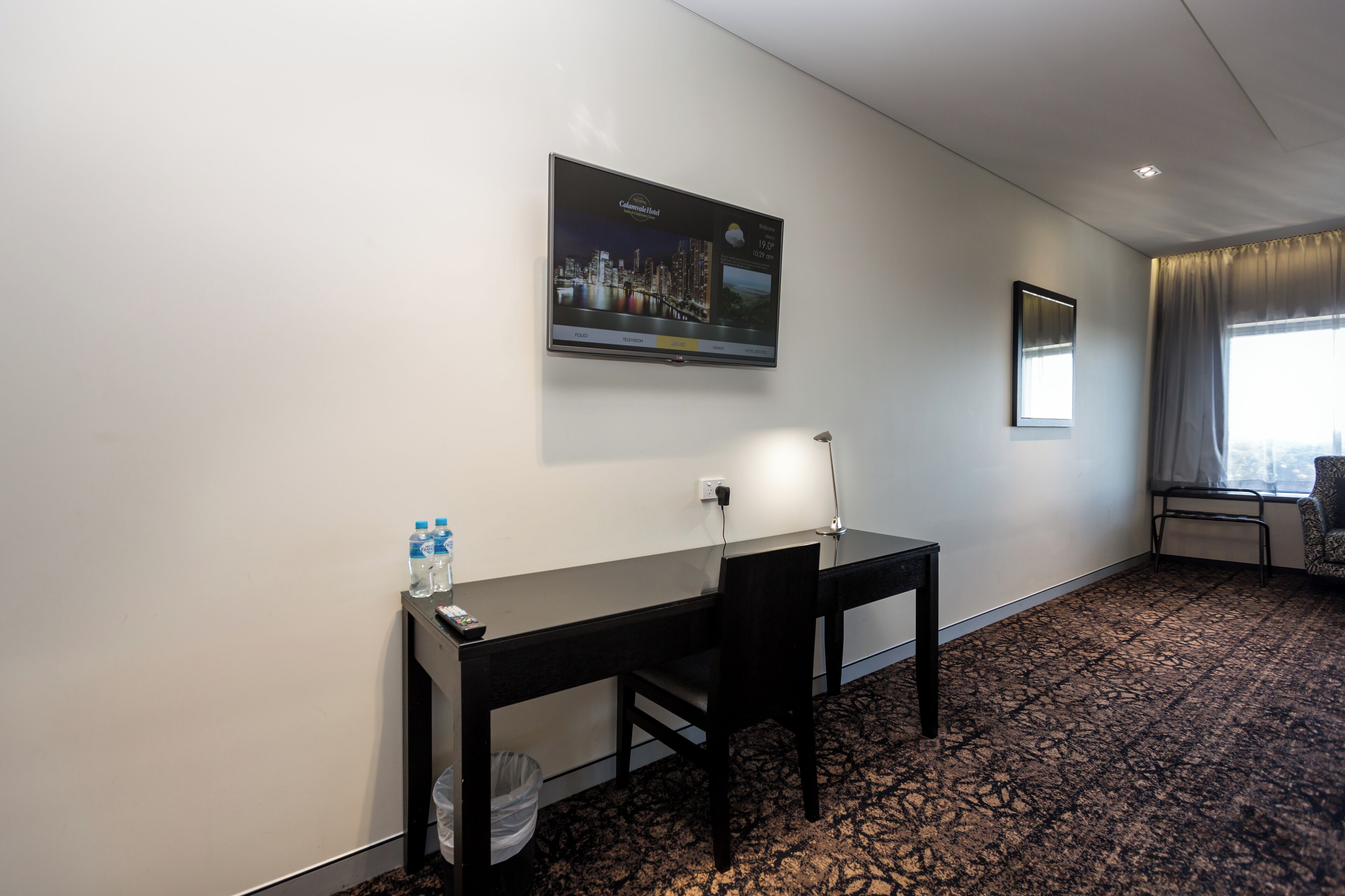 Una habitación de hotel con escritorio, silla y un amplio ventanal.