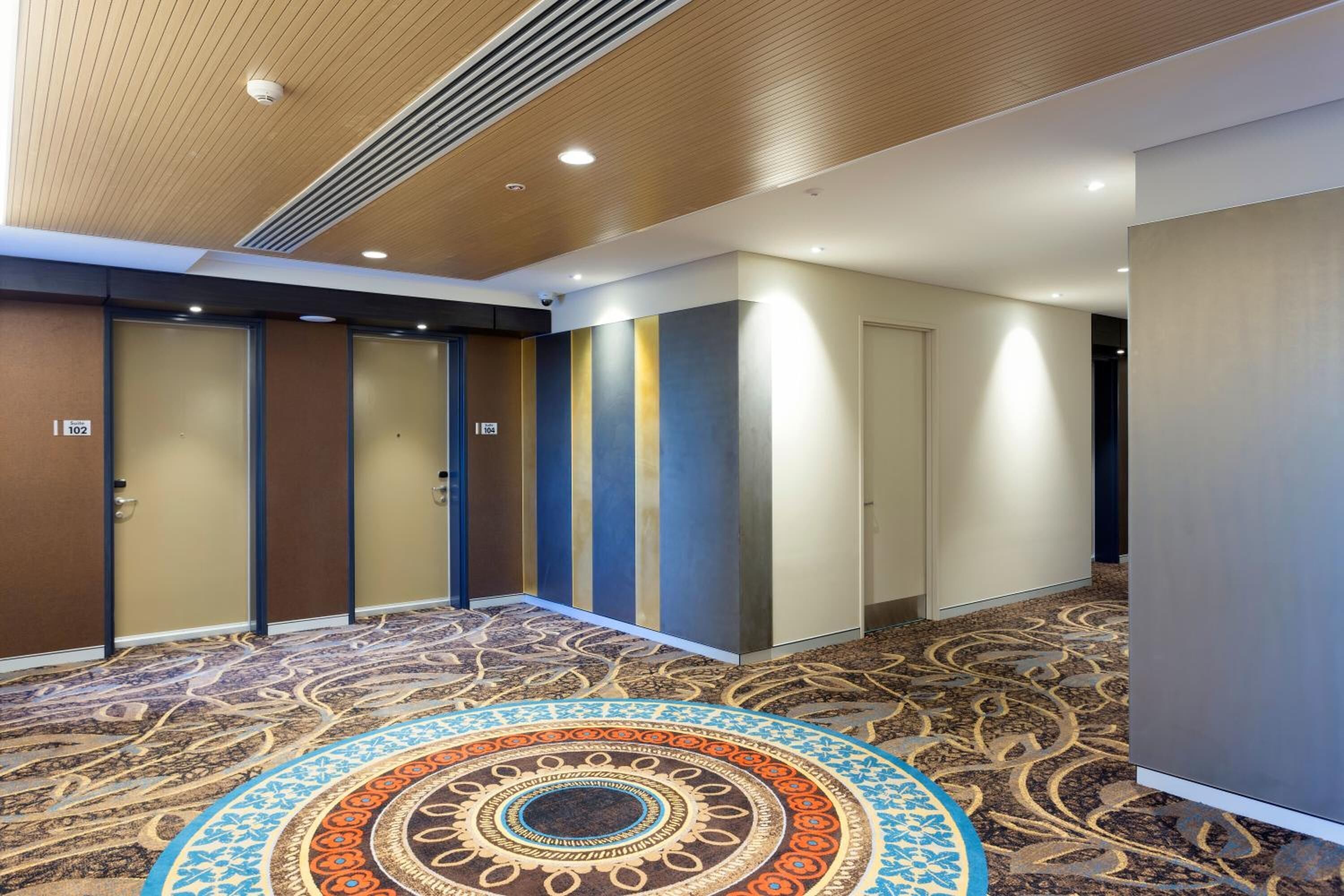 Un pasillo de hotel con alfombra estampada, techo de madera y puertas numeradas 102.