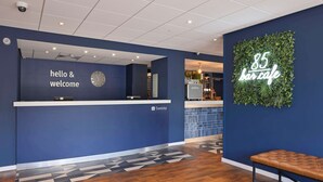 Et receptionsområde med et skilt der siger 'hello & welcome', et ur og Travelodge logo.