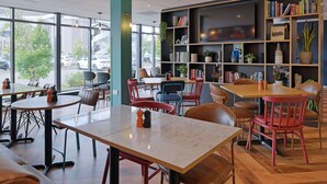 En moderne café med runde borde og stole, en reol med bøger og pynteting, og et stort TV ophængt på væggen.