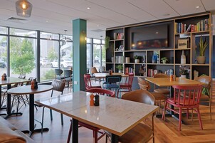 A modern cafe with round tables and chairs, a bookshelf with books and decorative items, and a large TV mounted on the wall.