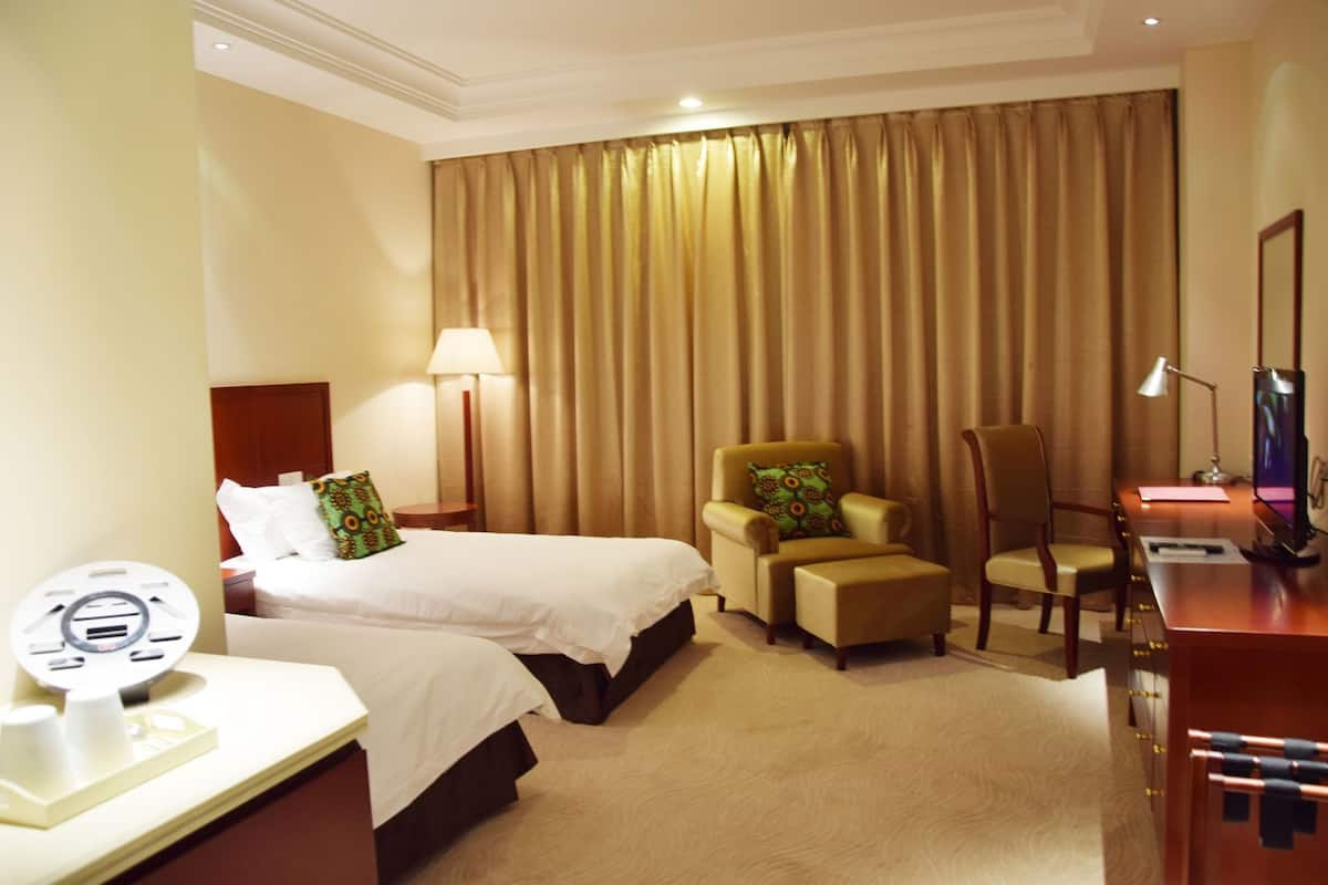A hotel room with two beds, a desk, a chair, a lamp, and a television.