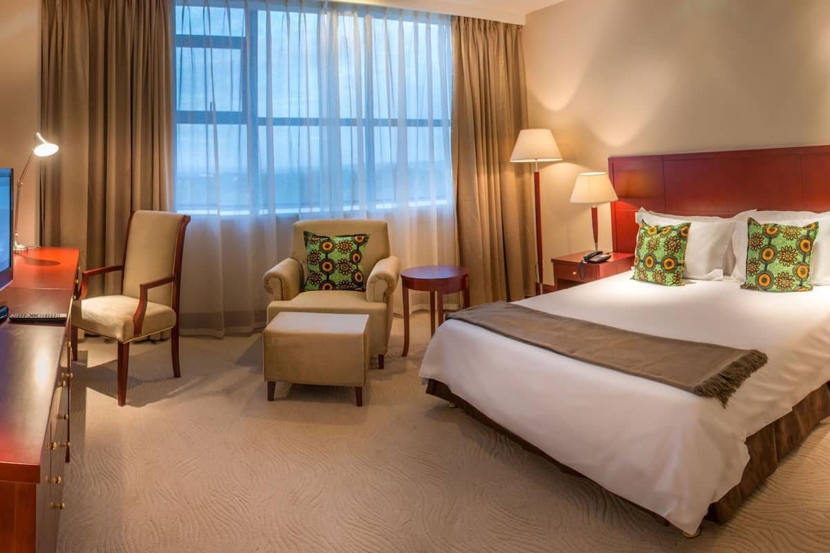 A hotel room with a bed, two armchairs, a small table, a TV, and a window with curtains.