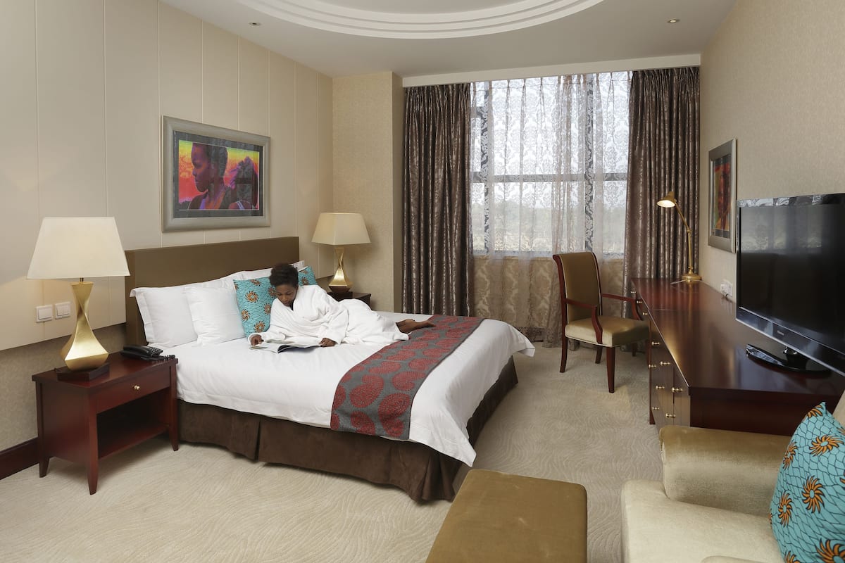 A hotel room with a bed, bedside tables, a desk, a chair, a television, and curtains.