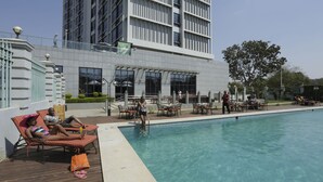 Zona de piscina con sillas de descanso, una piscina y un edificio moderno con grandes ventanales.