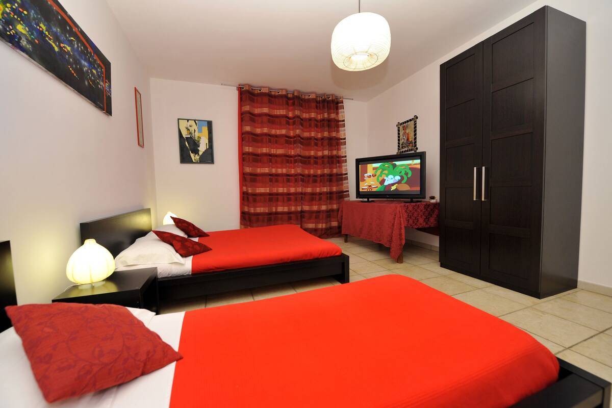 A hotel room with two beds, a TV, a wardrobe, and artwork on the walls.
