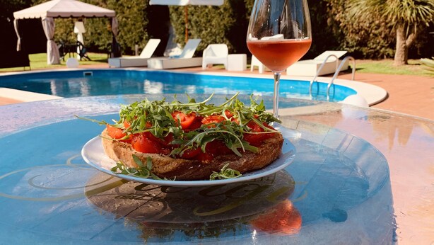 A glass table with a plate of food and a glass of red wine by a pool. - B&B A Casa di Joy (Lecce)