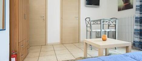 Un dormitorio con cama, una mesa con silla, un extintor y un radiador.