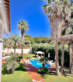 A pool area with a clear blue pool, surrounded by palm trees and a white building with a tiled roof. - B&B A Casa di Joy (Lecce)