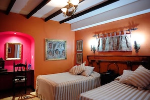 A room with two beds, a chair, a desk, and a mirror. There are paintings on the wall and a chandelier. - Hotel Casona Maya Mexicana (Tapachula)