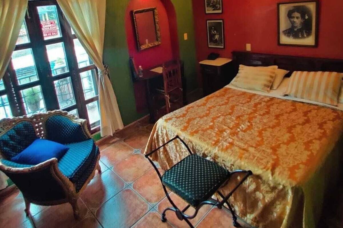 Ein Zimmer mit Bett, Stuhl, Schreibtisch und einem Fenster mit Vorhängen.