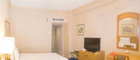 A hotel room with two beds, a desk, a television, a mirror, and a door leading to another room.