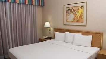 Habitación de hotel con una cama grande, una mesita de noche con lámpara, un cuadro en la pared y una ventana con cortinas.