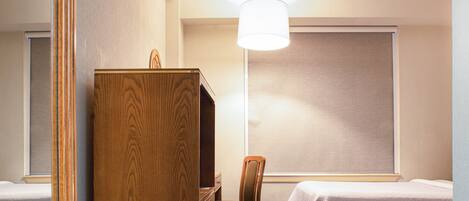 A hotel room with two beds, a wooden desk, a chair, and a large window with a blind.