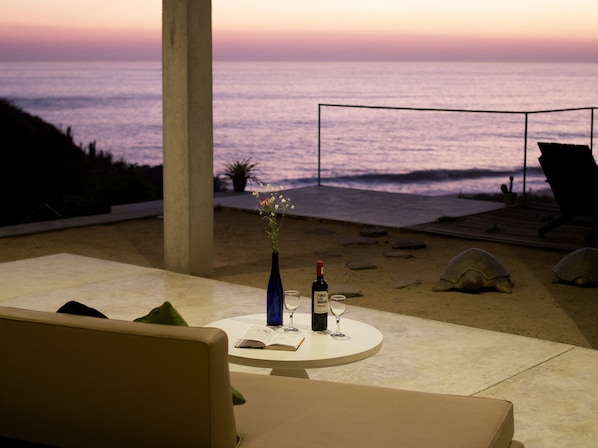 A table with a bottle of wine, a glass, and an open book, overlooking the ocean at sunset.