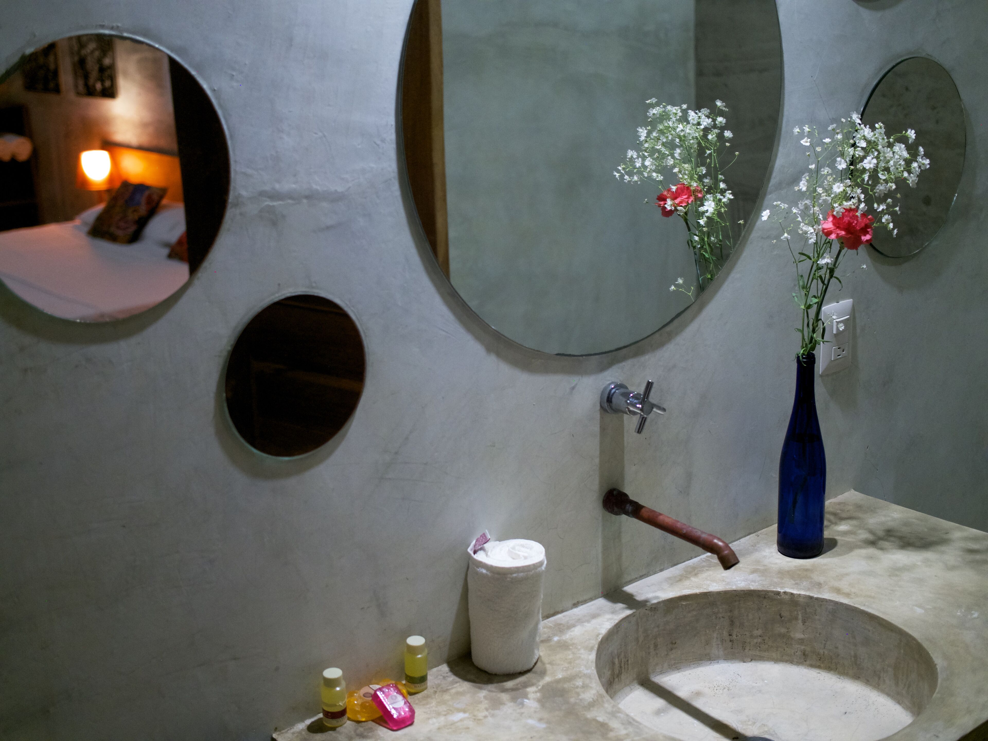 A bathroom with a large mirror, a sink, and a vase with flowers.