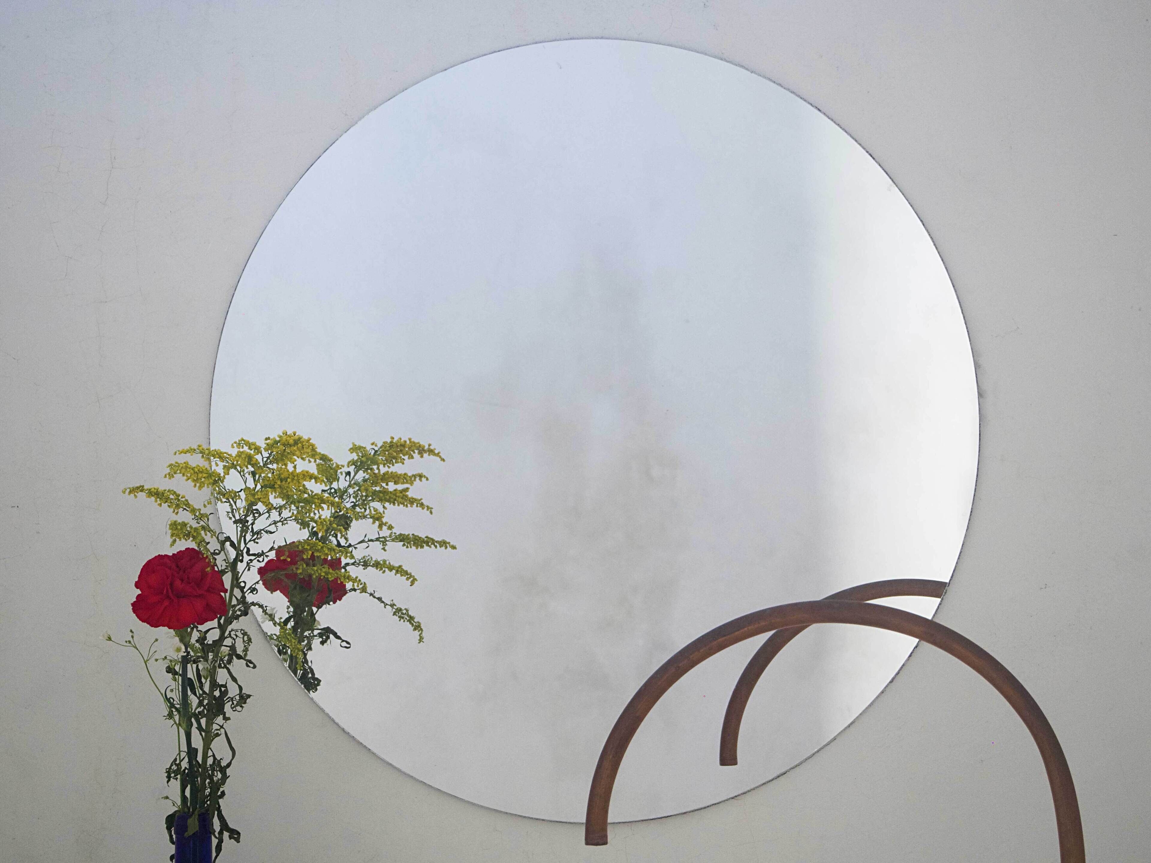 A circular mirror with a vase of flowers on a plain wall.