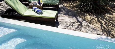 A poolside area with lounge chairs, a small table with a towel and a bottle, and a flower vase.