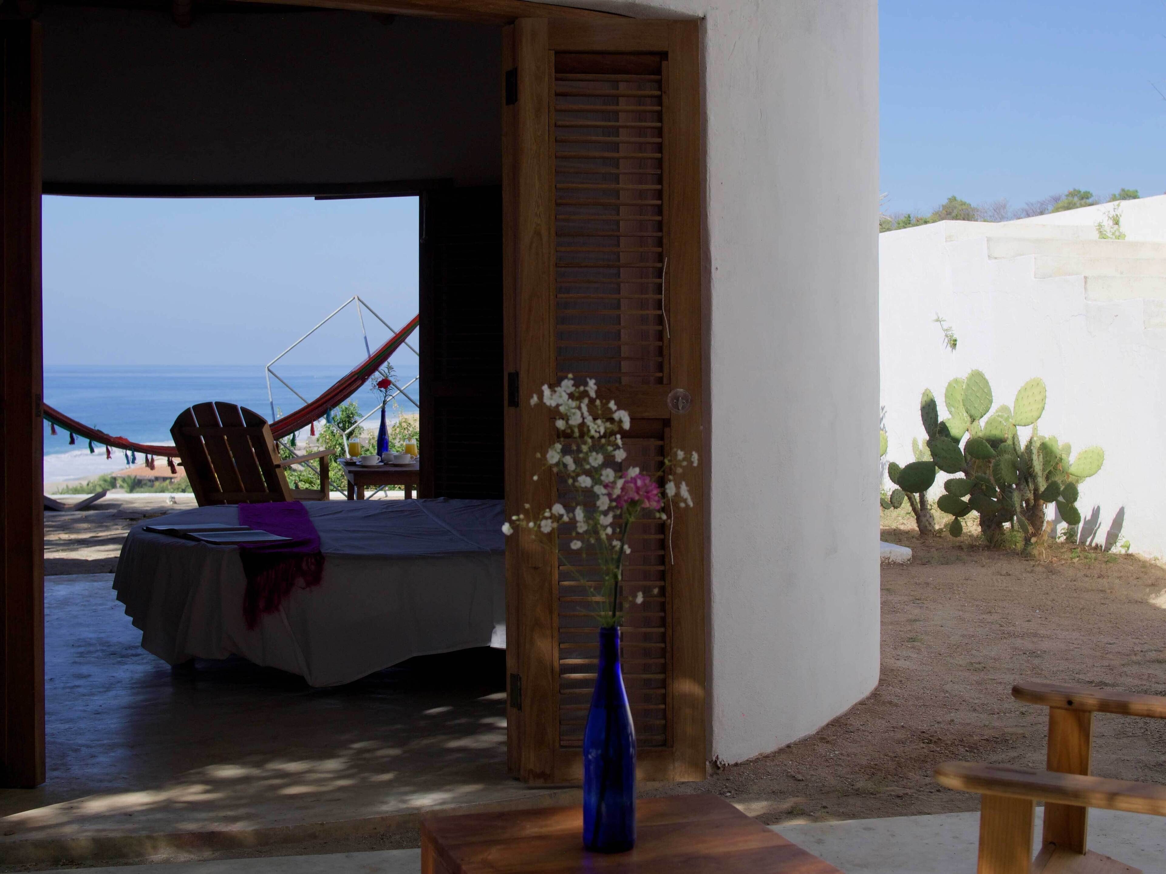 A bedroom with a view of the beach, a hammock, and a cactus plant.