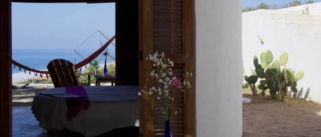 A bedroom with a view of the beach, a hammock, and a cactus plant.
