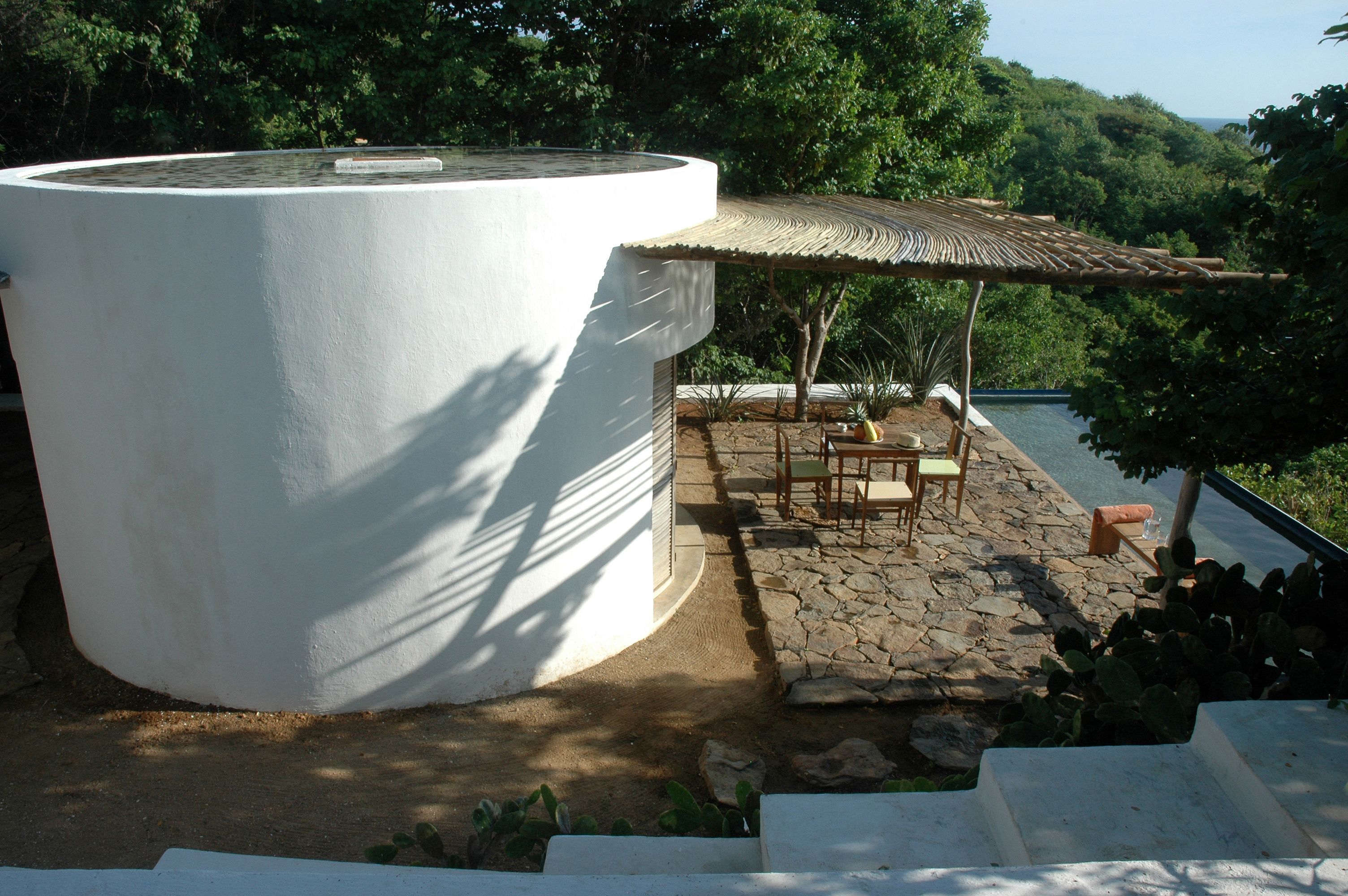 A white cylindrical structure, possibly a water tank, adjacent to a patio with a thatched roof and outdoor furniture.