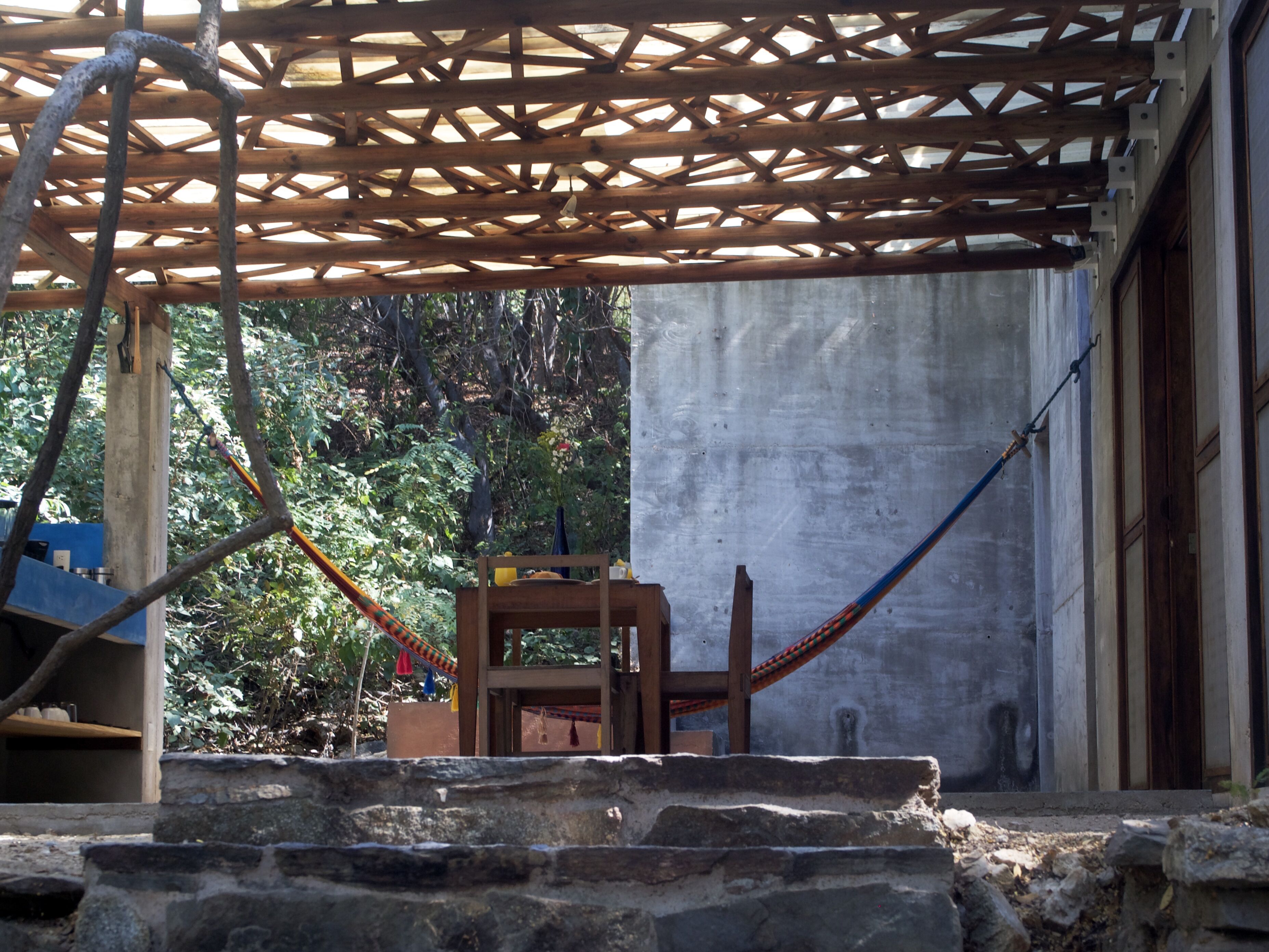 A covered outdoor area with a wooden structure, a concrete wall, and a hammock.