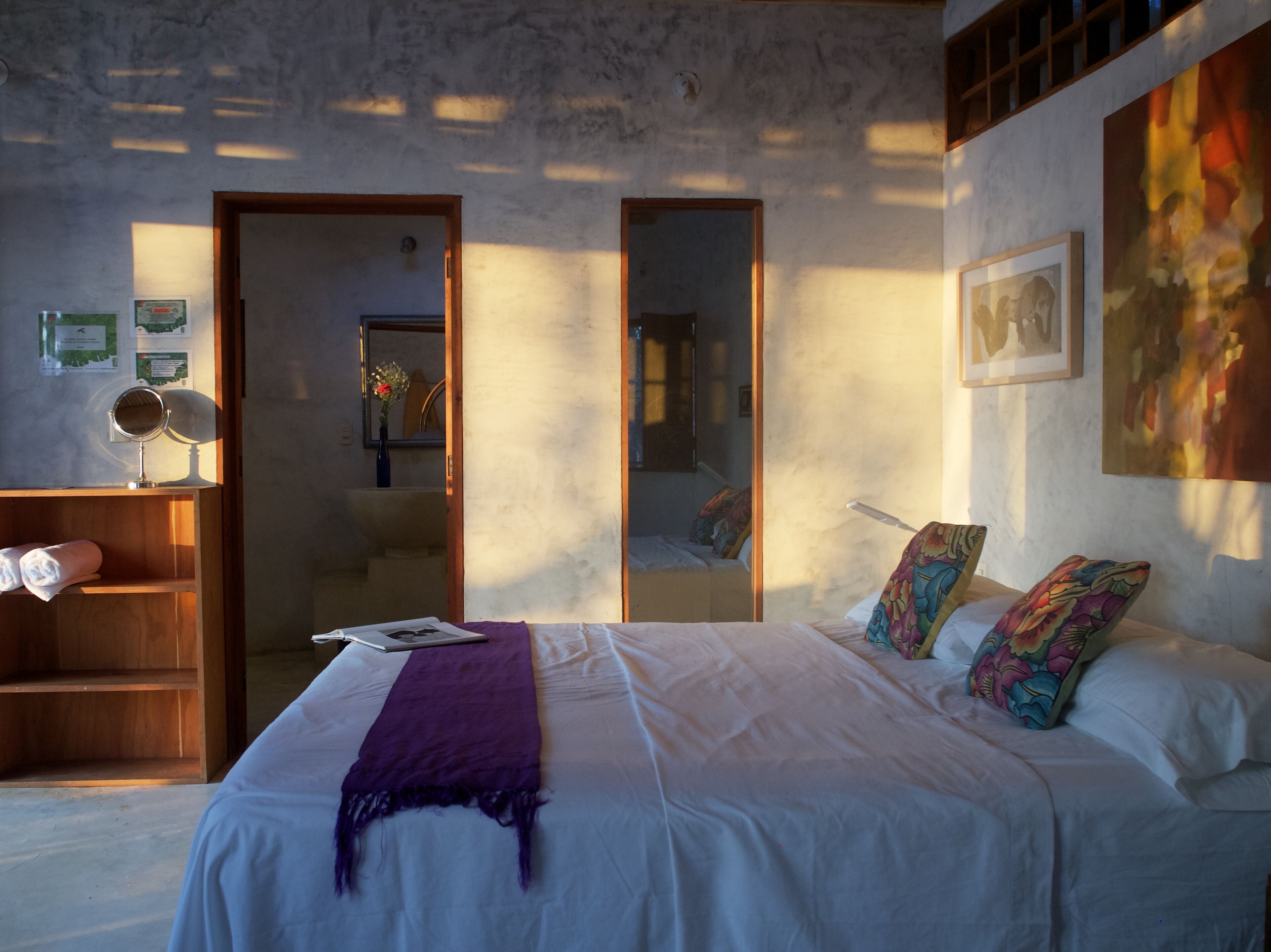 A bedroom with a bed, a wooden shelf, a mirror, a framed picture, and a window.