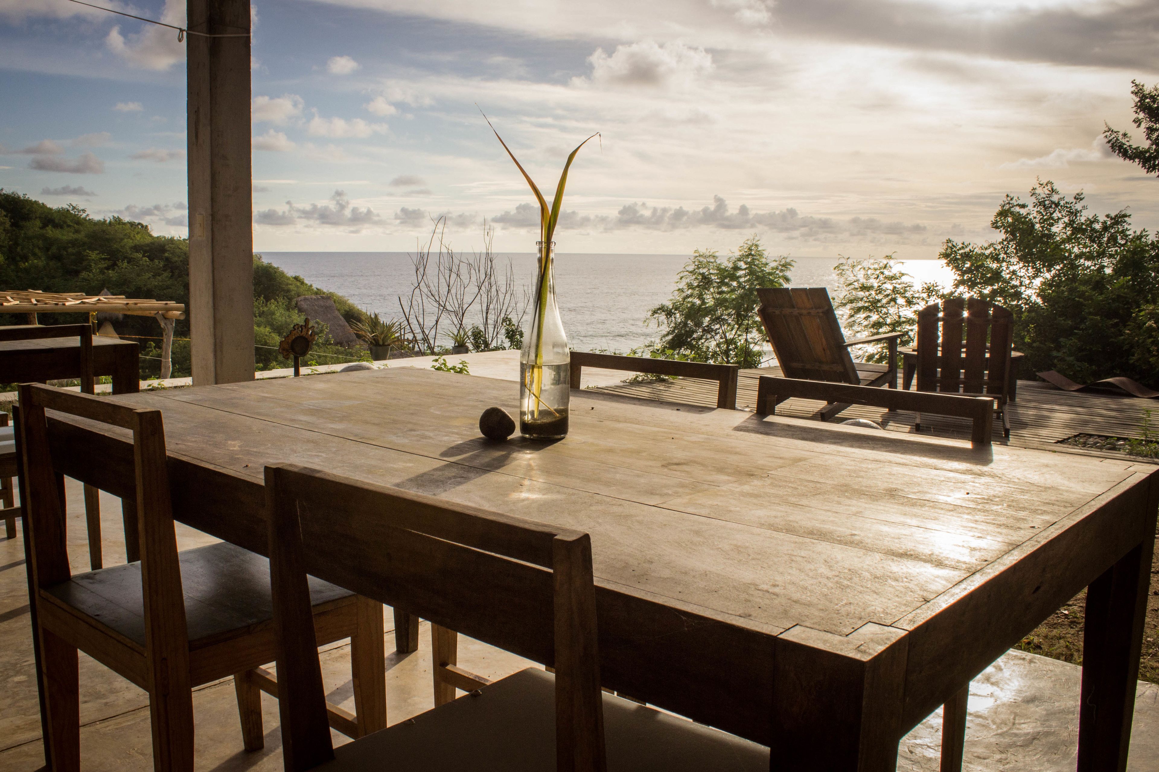 A wooden table with chairs, a vase with a plant, and a view of the sea.