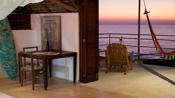 Una habitación con una mesa y sillas de madera, una hamaca, una tabla de surf y un cuadro en la pared.
