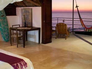 A room with a wooden table and chairs, a hammock, a surfboard, and a painting on the wall. - Casa Mermejita Mazunte (Santa María Tonameca)
