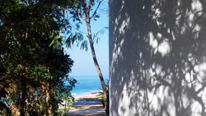 Un sendero que lleva a una playa con vistas al océano, rodeado de árboles y un muro blanco.