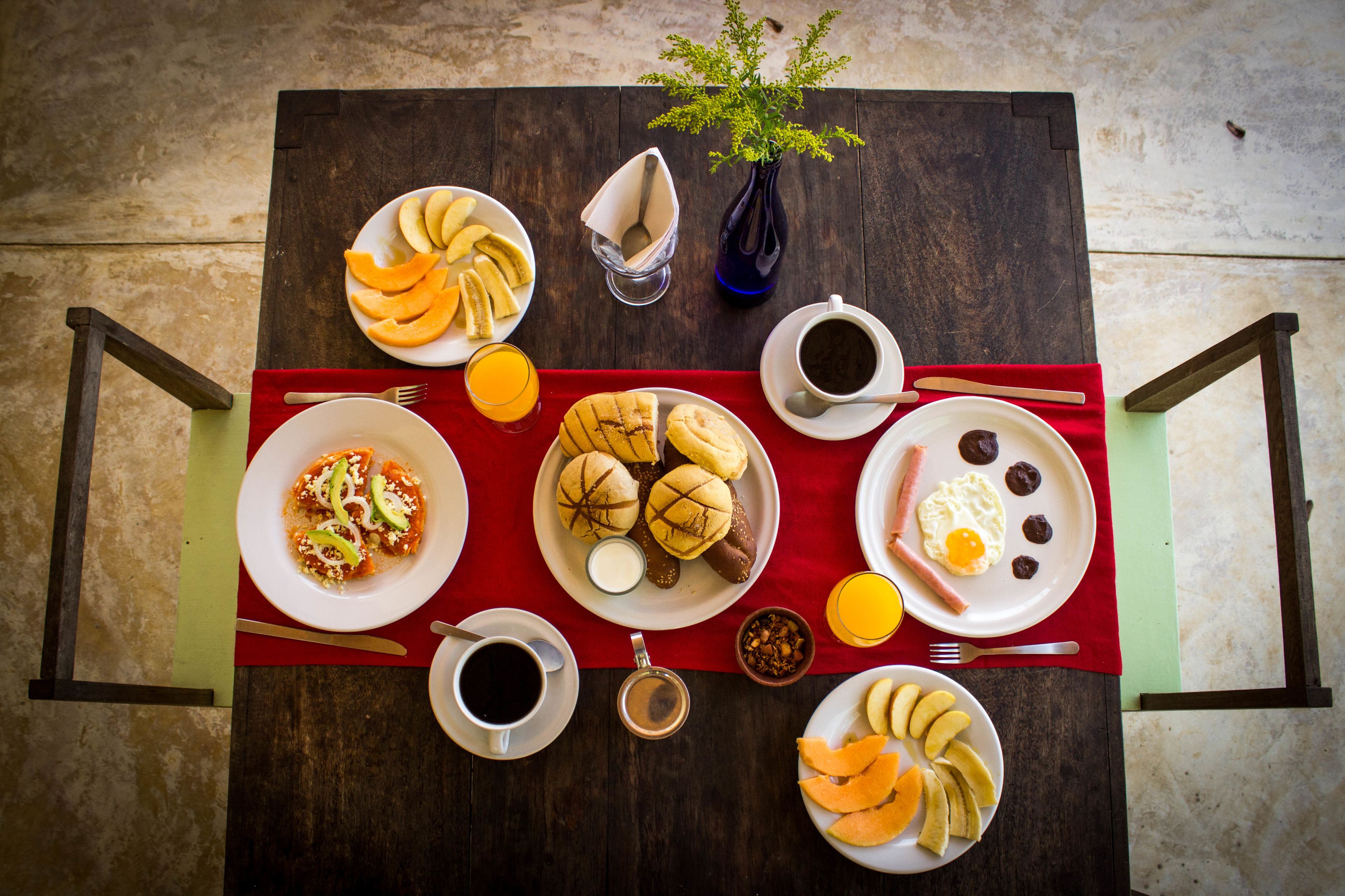 A breakfast table with plates of food, cups of coffee, a vase with a plant, and a red placemat.