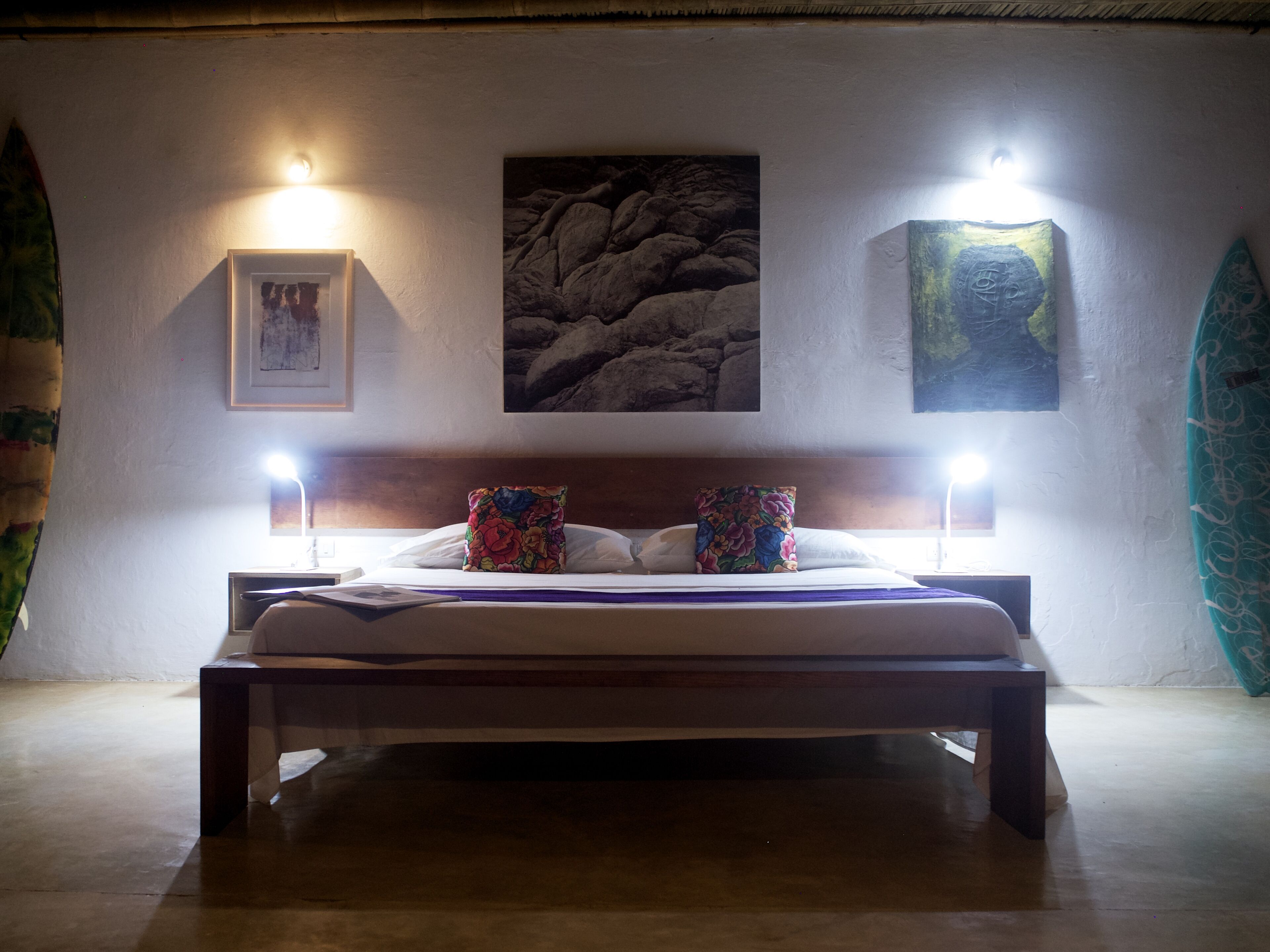 Un lit avec deux oreillers, une tête de lit et deux lampes fixées au mur. Deux tableaux encadrés sont accrochés au mur au-dessus du lit.