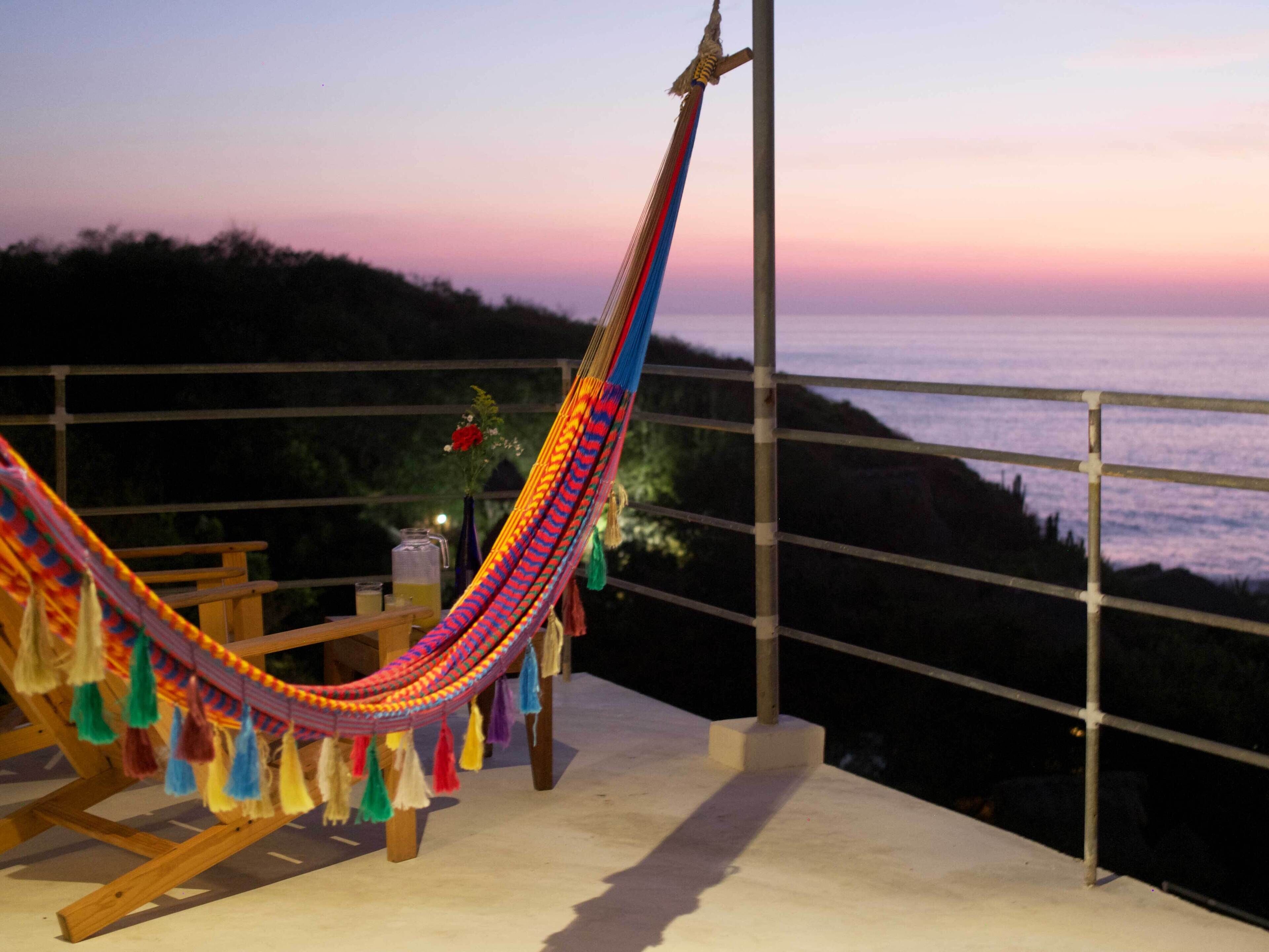 A hammock on a balcony with a view of the ocean at sunset.