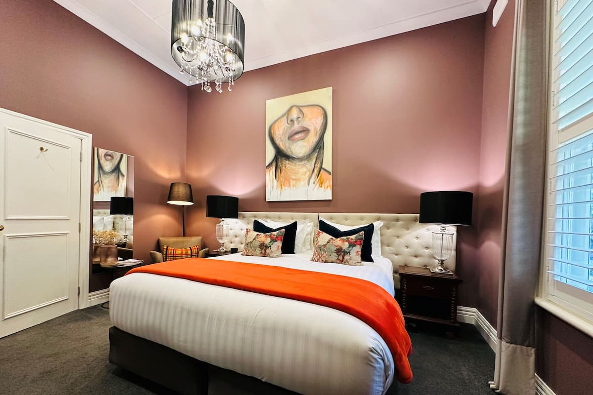 A bedroom with a large bed, two bedside tables, a chandelier, and artwork on the walls.